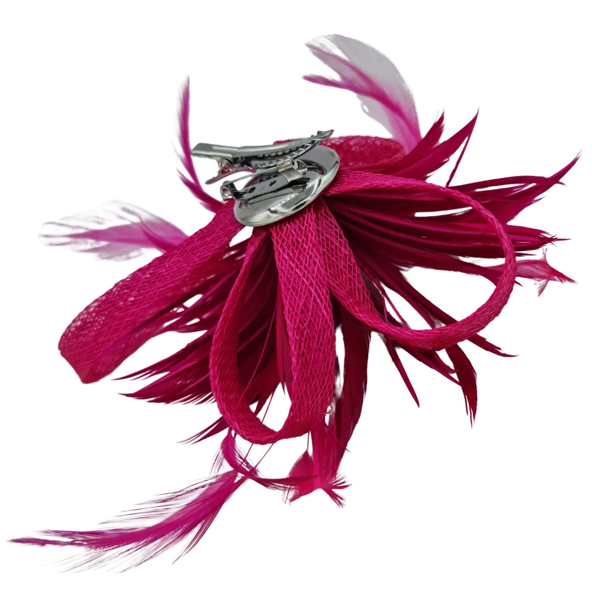 Broche-tocado de plumas en color fucsia . Mide 15 cm x 12 cm aproximadamente. En la parte trasera lleva metal plateado con alfiler para usarlo como broche y una horquilla para lucirlo en el pelo como un tocado. También puede lucirse decorando un bolso o un sombrero.