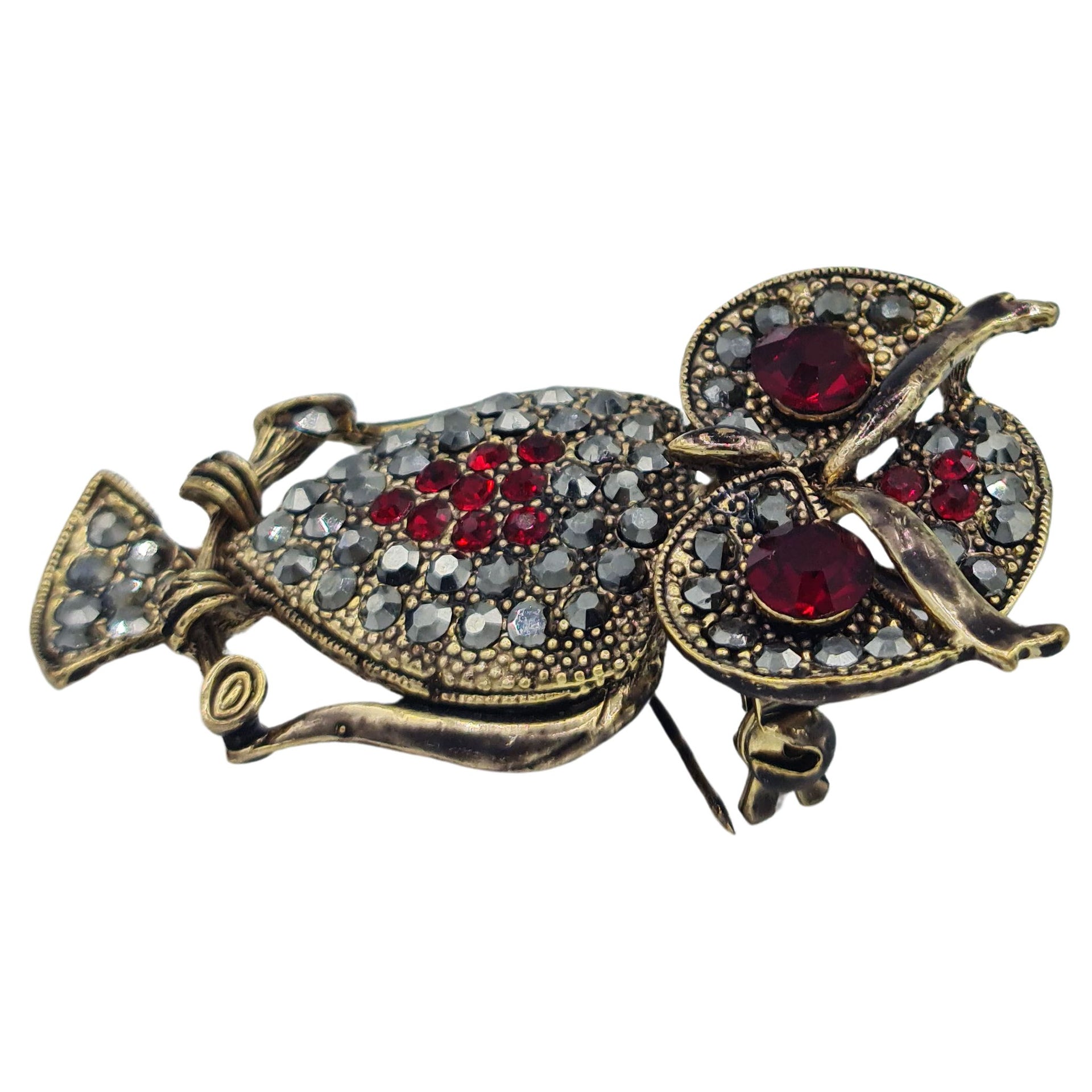 Broche buho colgante de metal dorado y brillantes de strass en color rojo. Trasera en color oro viejo con alfiler y seguro. Además del alfiler habitual, lleva una pieza que permite usarlo como colgante. Mide 6 cm de largo x 3 cm de ancho.