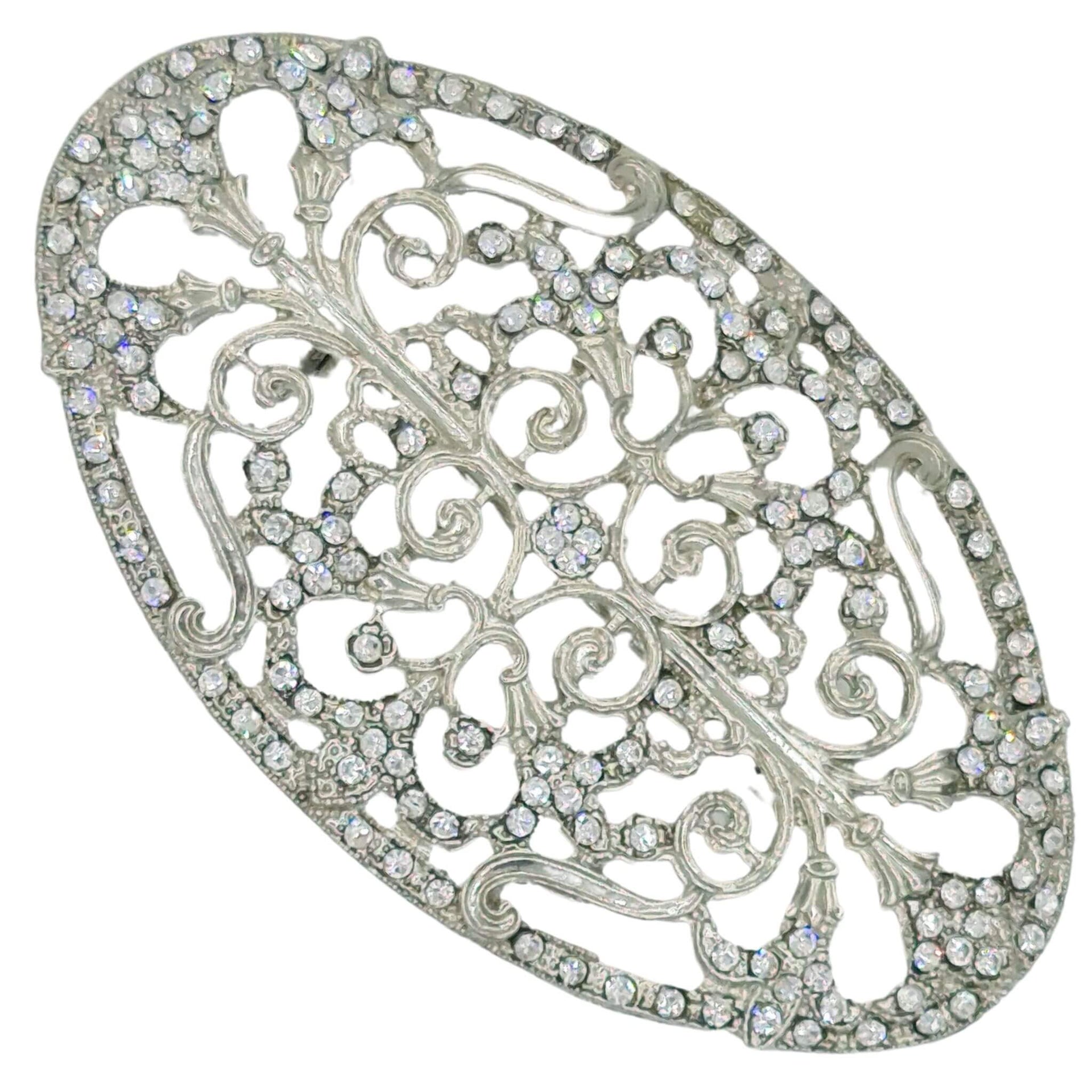 Broche ovalado en metal plateado y brillantes de strass en color blanco. Mide 8 cm de largo por 5 cm de ancho.El alfiler trasero es de 6 cm con cierre de seguridad. Un complemento ideal para lucir como broche sobre la ropa, un bolso, un sombrero o un collar.