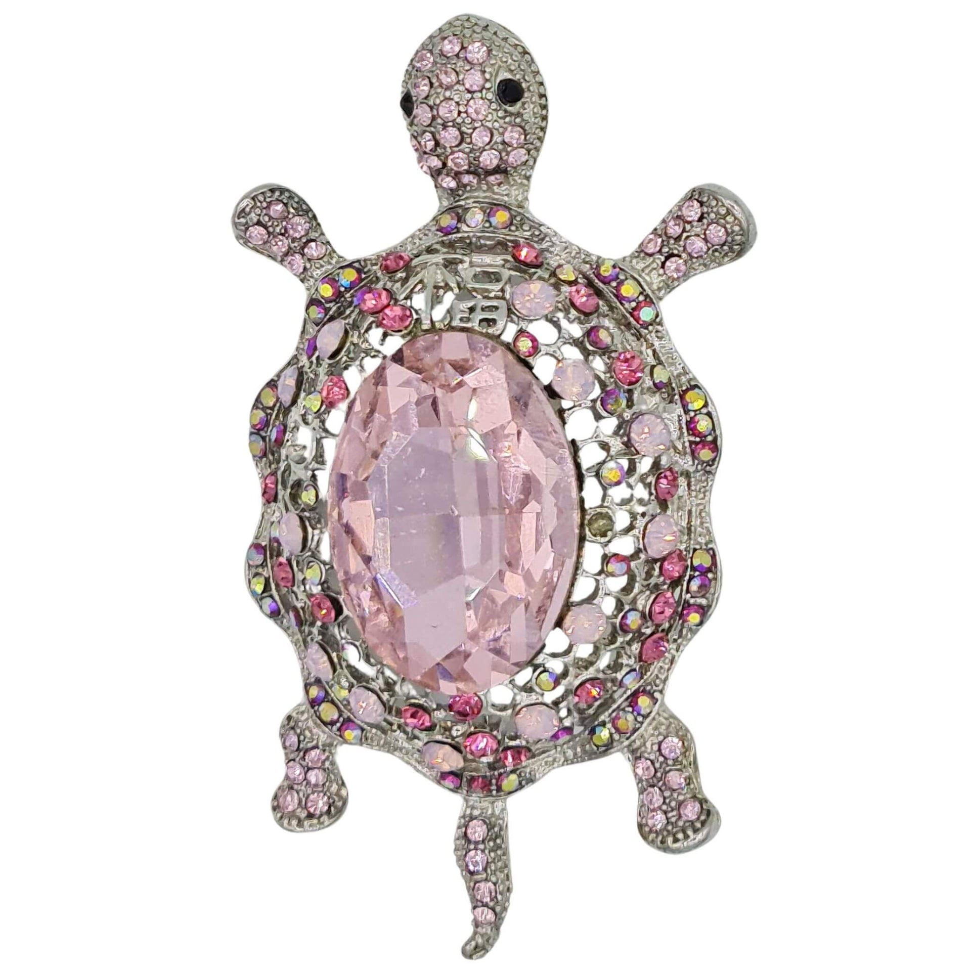 Broche de tortuga con brillantes rosas de strass y metal plateado en la parte trasera. Puede usarse también con una cadena como colgante ya que lleva una argolla en la parte superior. Mide 8 cm de largo x 5 cm de ancho.