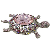 Broche de tortuga con brillantes rosas de strass y metal plateado en la parte trasera. Puede usarse también con una cadena como colgante ya que lleva una argolla en la parte superior. Mide 8 cm de largo x 5 cm de ancho.