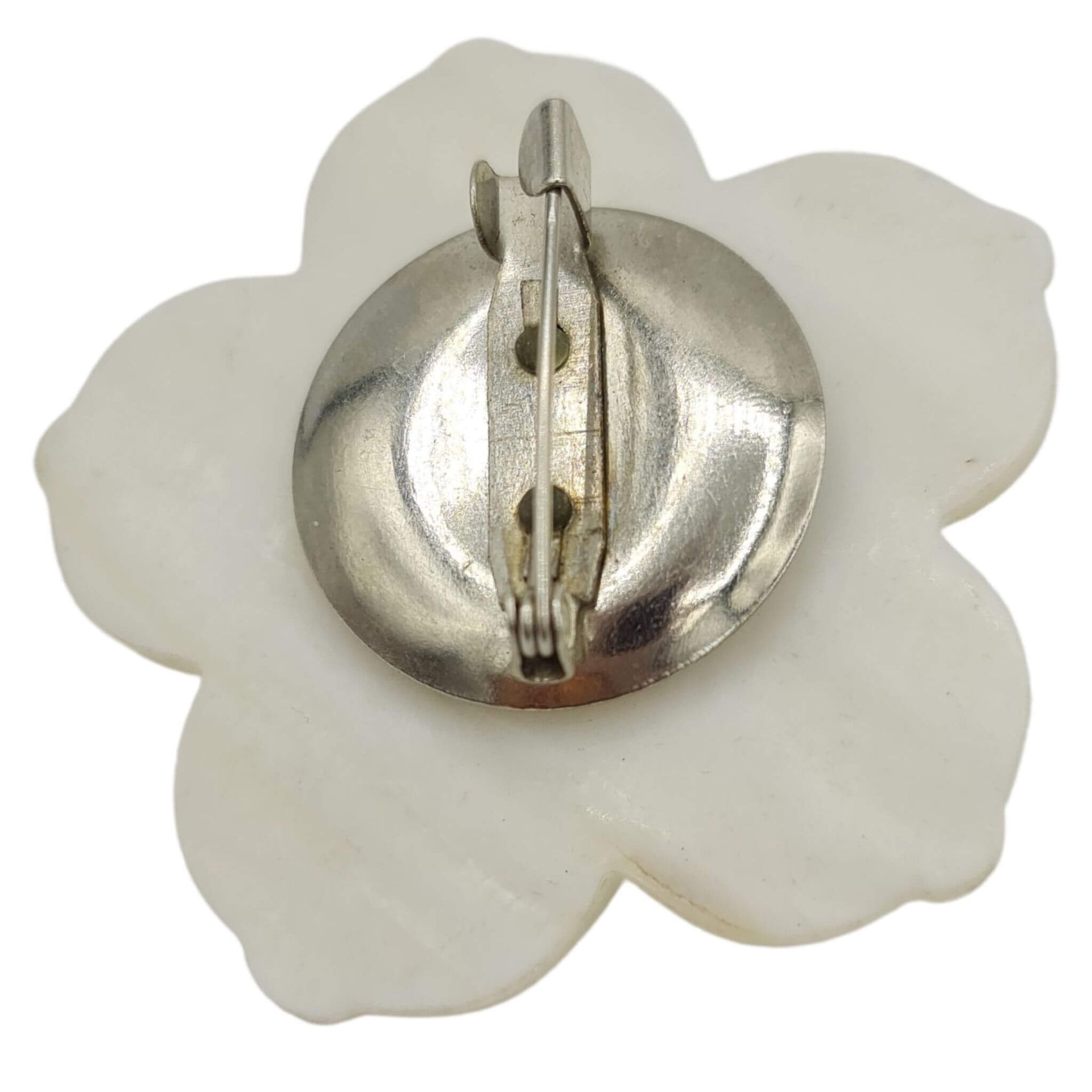 Broche flor nacarada en blanco con central de pequeñas bolitas en color lila. Trasera en metal plateado. Mide 5 cm en su parte más ancha.