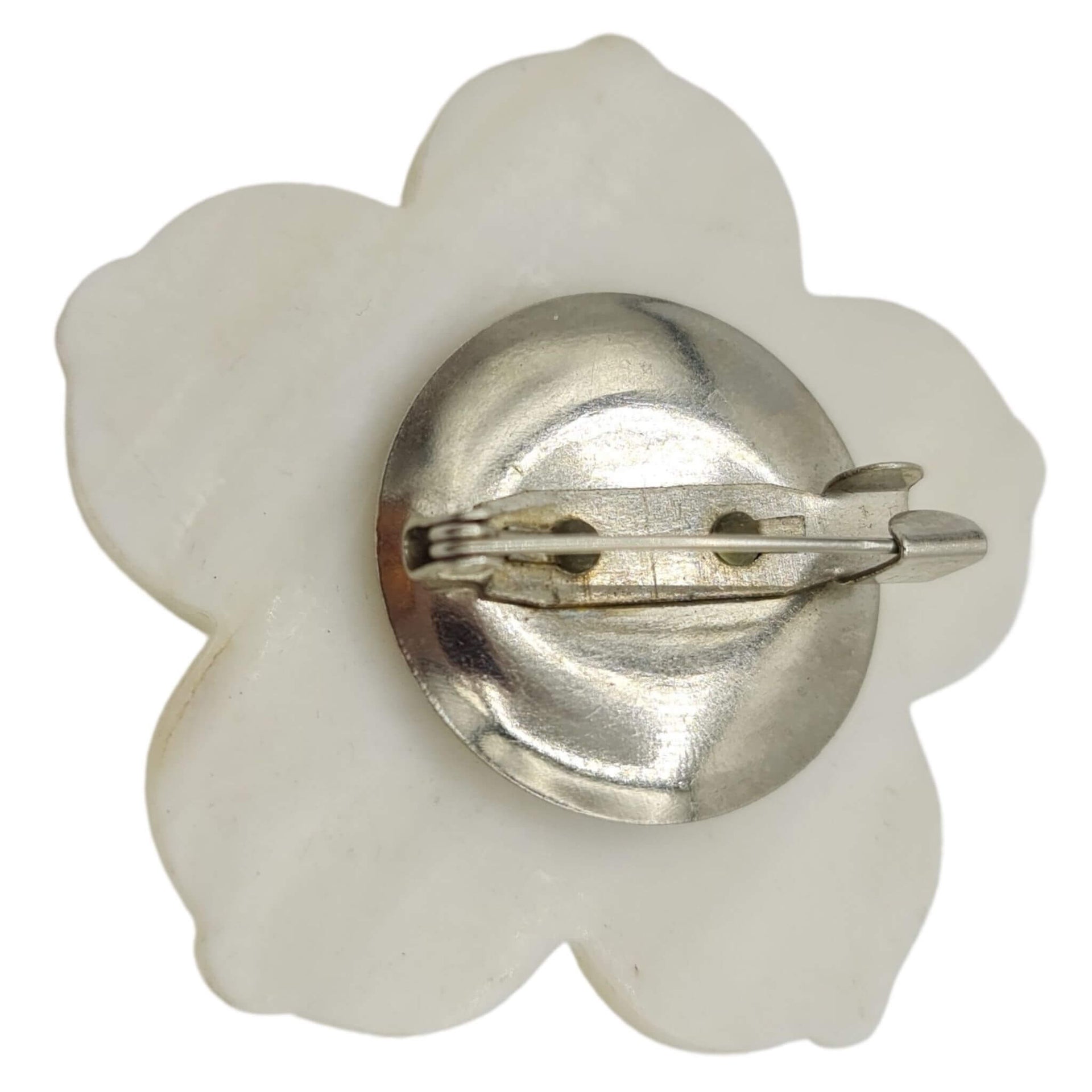 Broche flor nacarada en blanco con central de pequeñas bolitas en color lila. Trasera en metal plateado. Mide 5 cm en su parte más ancha.