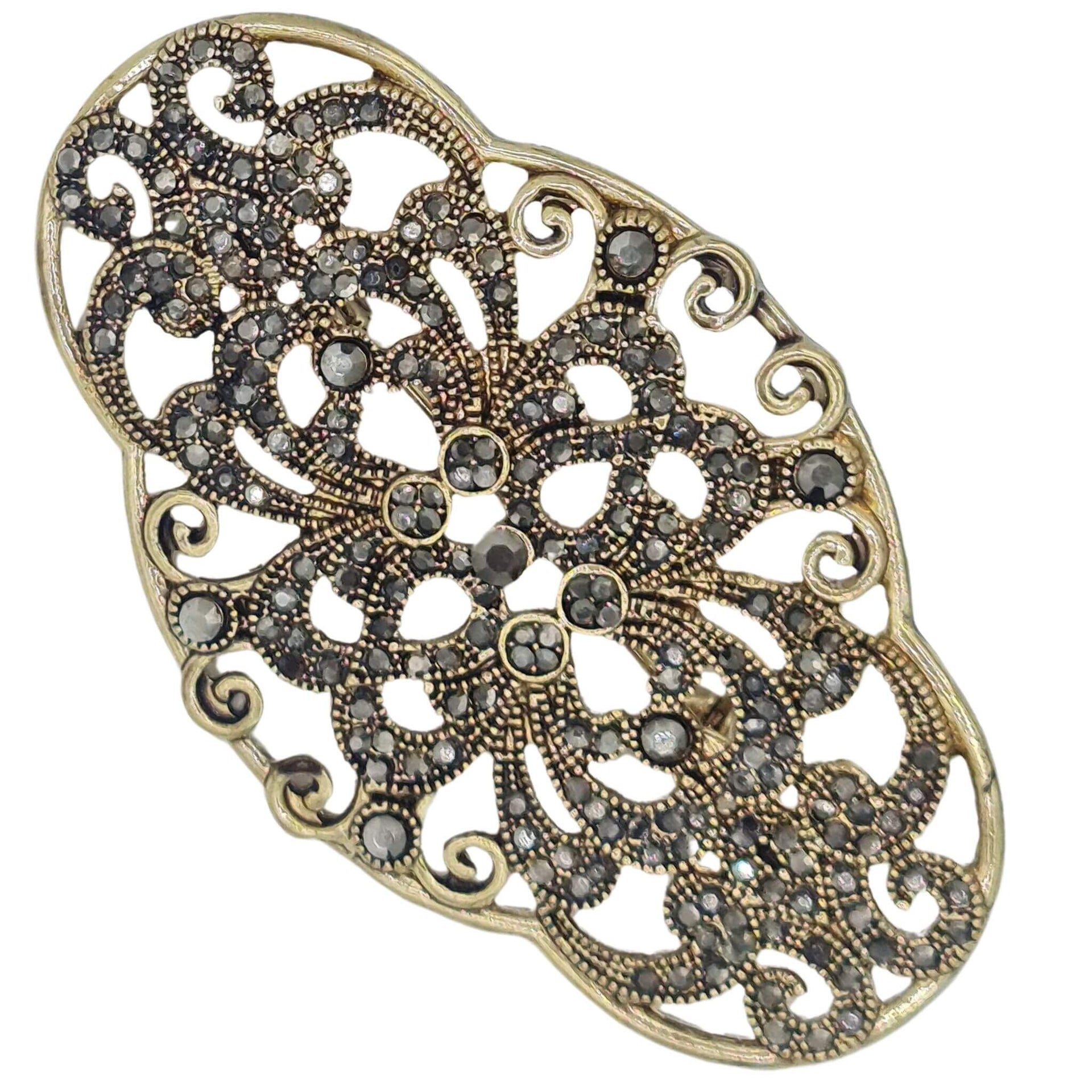 Broche metal dorado y brillantes de strass en gris oscuro. Mide 8 cm de largo por 4 cm de alto. El alfiler trasero es de 6 cm con cierre de seguridad.