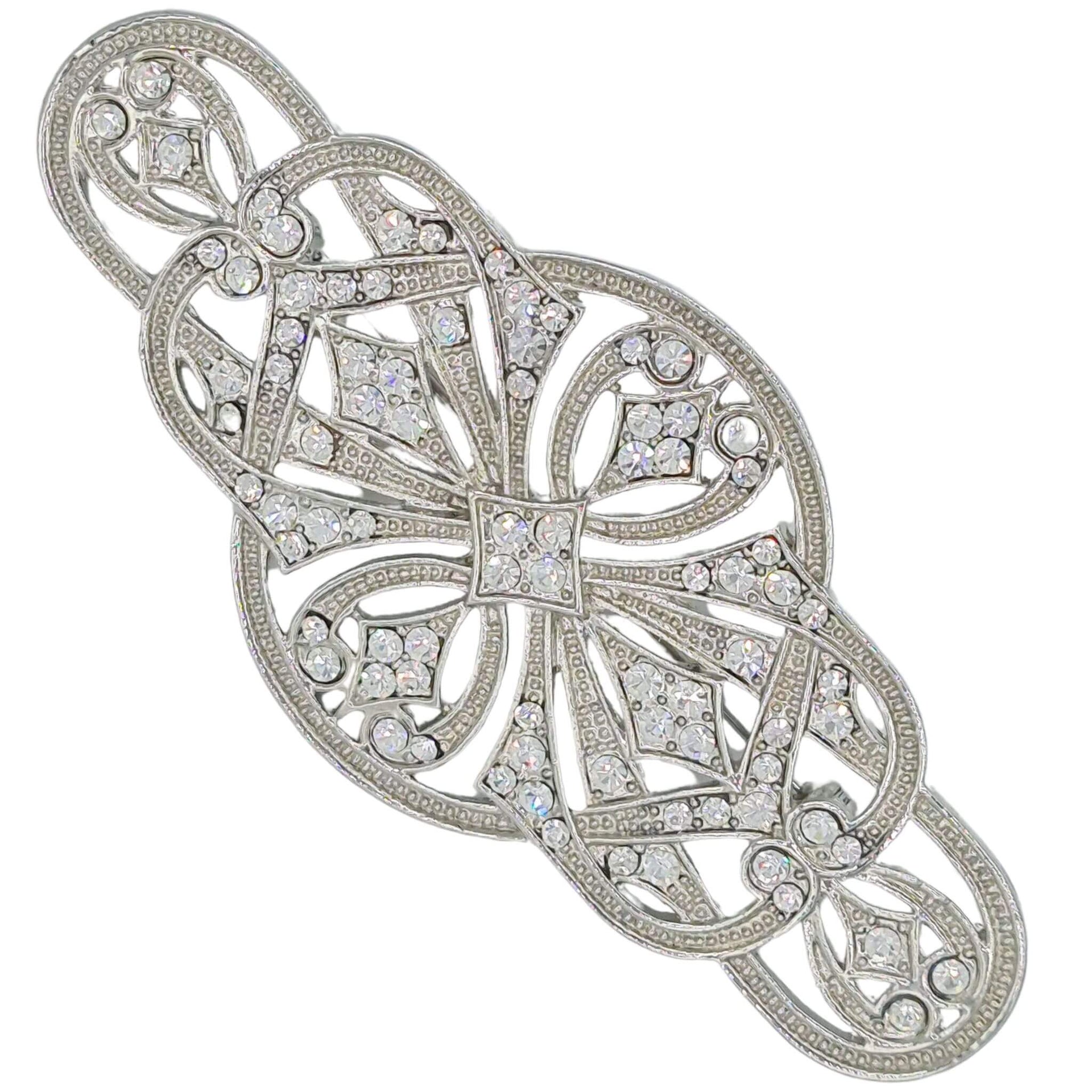 Broche alargado en metal plateado y brillantes de strass en color blanco. Mide 9 cm de largo por 4 cm de ancho. El alfiler trasero es de 6 cm con cierre de seguridad. Un complemento ideal para lucir como broche sobre la ropa, un bolso, un sombrero o un collar.