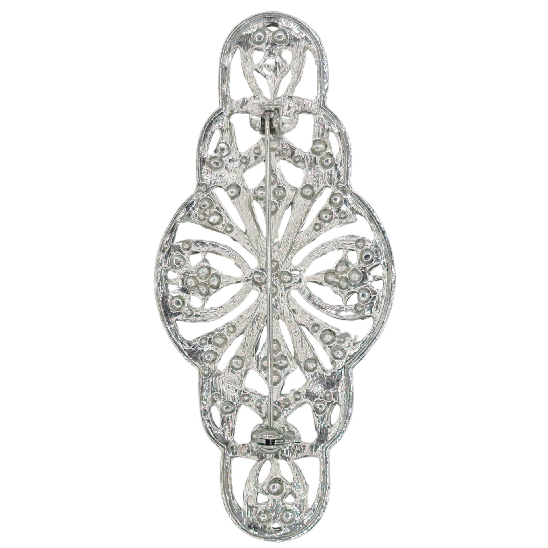 Broche alargado en metal plateado y brillantes de strass en color blanco. Mide 9 cm de largo por 4 cm de ancho. El alfiler trasero es de 6 cm con cierre de seguridad. Un complemento ideal para lucir como broche sobre la ropa, un bolso, un sombrero o un collar.