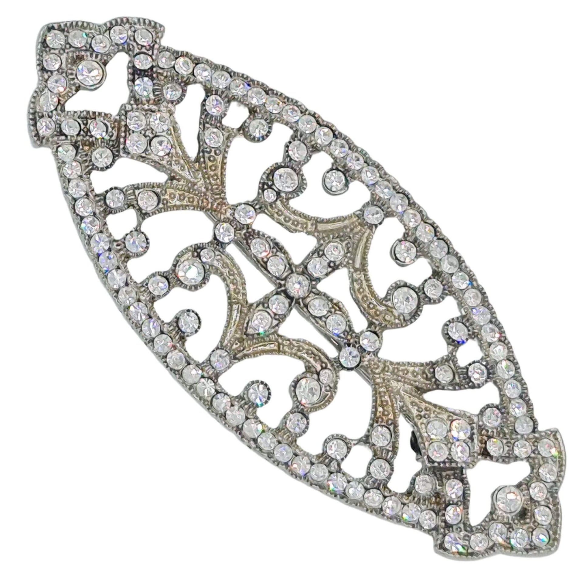 Broche ovalado en forma de pera en metal plateado y brillantes de strass en color blanco. Mide 7 cm de largo por 3 cm de ancho. El alfiler trasero es de 5 cm con cierre de seguridad. Un complemento ideal para lucir como broche sobre la ropa, un bolso, un sombrero o un collar.