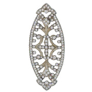 Broche ovalado en forma de pera en metal plateado y brillantes de strass en color blanco. Mide 7 cm de largo por 3 cm de ancho. El alfiler trasero es de 5 cm con cierre de seguridad. Un complemento ideal para lucir como broche sobre la ropa, un bolso, un sombrero o un collar.